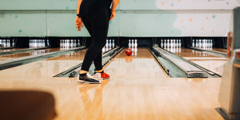 Woman rolling red ball down lane towards pins at 10 pin bowling alley