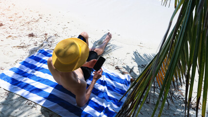 Domad Digital young man in hat with smart phone  as sunbathing on the beach