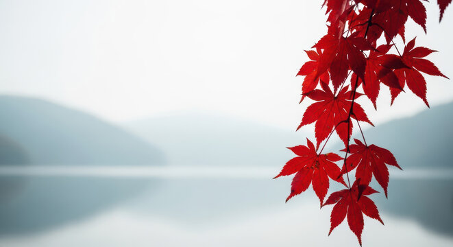 Vibrant red maple leaves grace a serene misty lake and mountain landscape