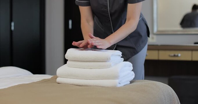 Woman hands in a hotel room lay out fresh and clean towels for guests. Hotel service concept.