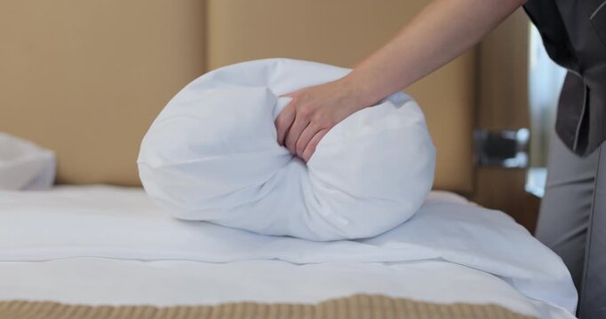 Close-up of young maid in uniform, fluffing pillows and punching them into shape. Hotel cleaning concept.