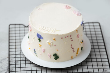 Beautiful birthday cake with white chocolate icing on the grey pastel background decorated with cream flowers