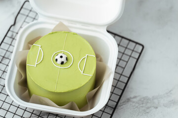 Cute little bento cake with green cream cheese frosting decorated with football ball on the field...