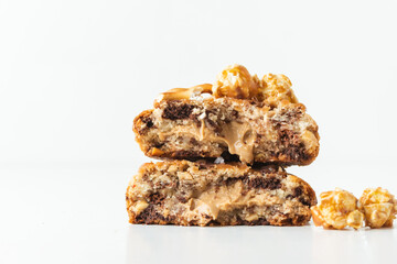 Close up shot of broken in half fresh chocolate American chip cookie decorated with salted camel and caramel popcorn. Cookies with peanut butter filling inside on the white background.