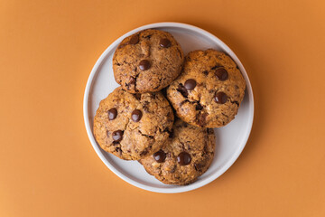 Stack of fresh chocolate American style chip cookies with nuts and chocolate drops on warm brown...