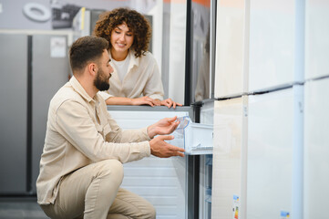 Couple choosing refrigerator in electronics store examining freezer compartment