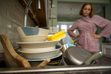 Procrastination, dirty dishes in kitchen, sad woman in the background