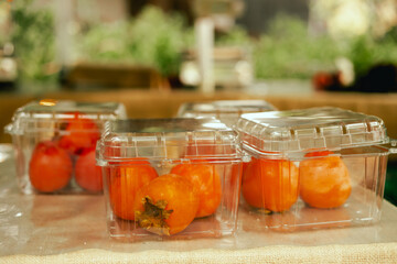 Fresh persimmon in plastic packaging at local urban market. Organic produce on sale at outdoor...