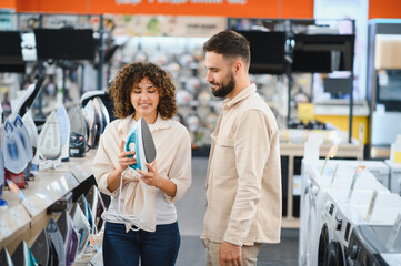 Couple choosing iron in electronics store, woman holding modern appliance, considering purchase...
