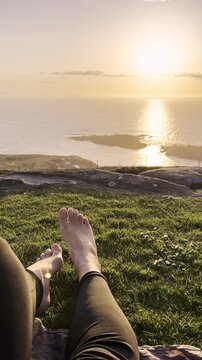 Feet resting on a grassy hill with mate during coastal sunset