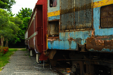 Close-up of an old locomotive and old carriages on a decommissioned railway, the paint cracked, peeled and rusted.