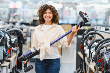 Woman choosing cordless vacuum cleaner in electronics store