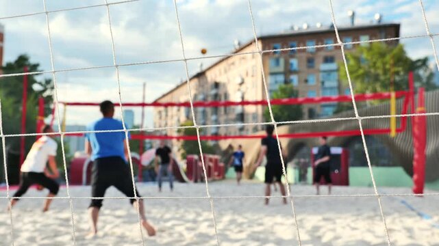 A group of young men are playing beach volleyball in a large city.
