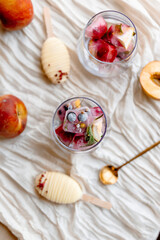 Glass filled with ice cubes made from berries, citrus, and mint — a refreshing, colorful base for summer drinks or fruity popsicles. Bright, airy composition with fruit in the background.