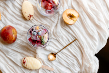 a clear glass filled with fruity ice cubes made from blackcurrants, orange slices and mint leaves. Summer treat prep with popsicle ingredients nearby.