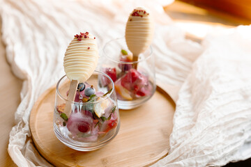 Ice cream on a stick standing inside a glass filled with berry ice cubes, citrus slices and mint leaves. A creative and refreshing summer dessert served in a drinkable, edible style.