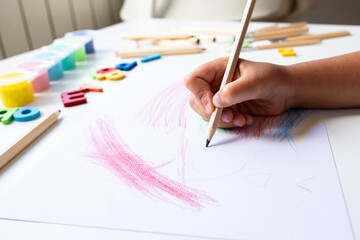 Child drawing with colored pencils on white paper at home