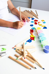 Child creating colorful art with pencils and magnetic letters on a white table