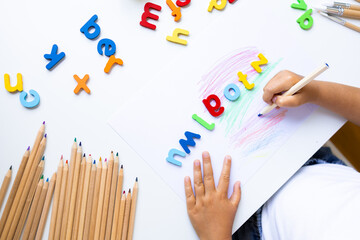 Child learning alphabet with colored pencils and foam letters on white table