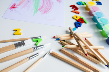 Colorful art supplies. Pencils, brushes, paints, and alphabet letters on table
