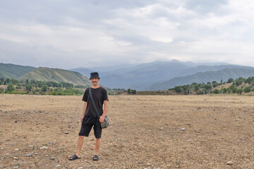 Asian senior man standing with mountains in background on cloudy summer day