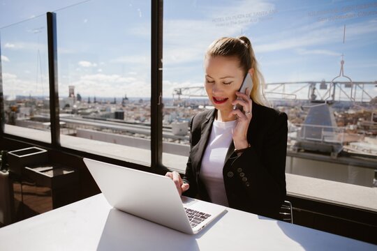 Businesswoman working on laptop and talking on phone in madrid rooftop terrace