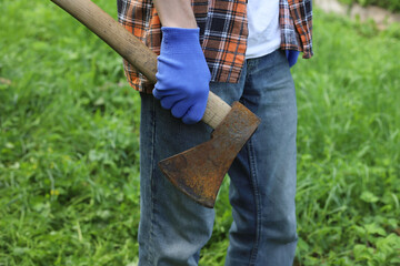 Work in the village. A guy in a checkered orange shirt and blue work gloves chops wood