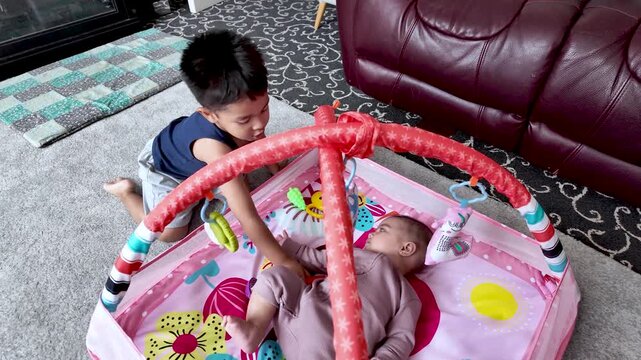 Brother and baby sister playing together at home on a colorful playmat