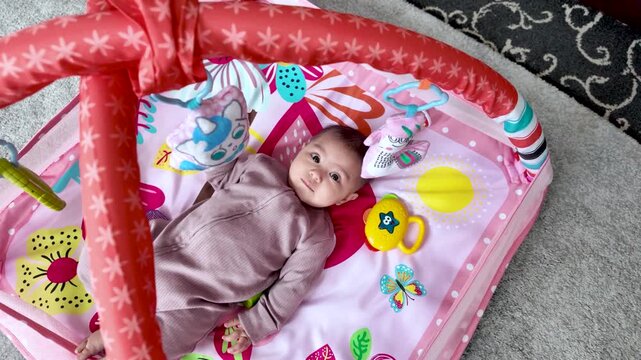 Six month old south asian baby girl lying on a colorful playmat, having fun with toys