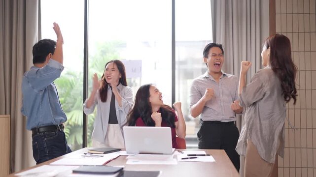 Asian business team achieves project success celebrating triumphantly at modern office workspace collaborative teamwork victory