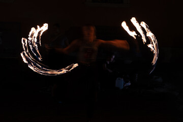 An anonymous street performer juggles with fire, creating beautiful orange light paintings against the black of night in a long exposure abstract shot.