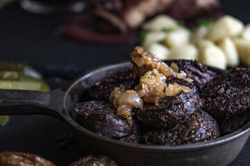 Close-up of Polish kaszanka blood sausage with fried onions in a cast iron pan. Concept of rustic Eastern European cuisine and dark food photography.