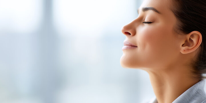 Woman with closed eyes taking a deep breath and enjoying a moment of calm and relaxation in soft natural light.