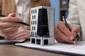 Real estate agent working with client at desk with house model in office, closeup
