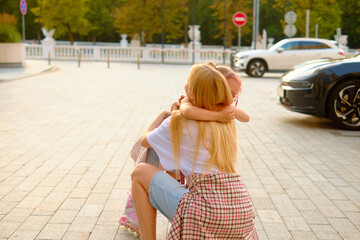 Heartwarming moment of mother and daughter hugging outdoors at sunset, capturing closeness and affection in a beautifully lit city park setting