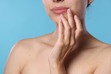 Young woman with lip balm on her lips against light blue background, closeup
