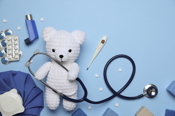 Pediatrics concept. Toy bear with stethoscope, thermometer and pills on light blue background, flat...