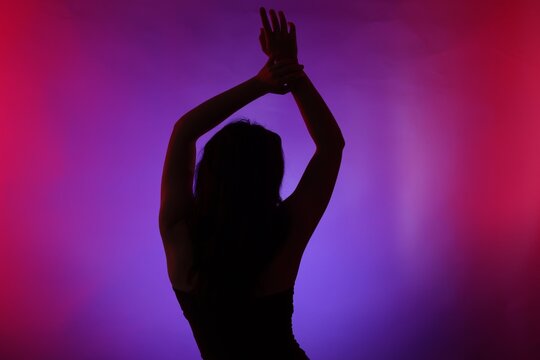 Silhouette of woman posing in neon lights on color background, back view