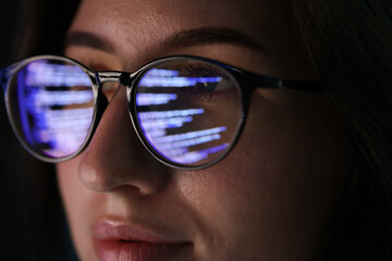 Young woman wearing glasses with reflection on dark background, closeup
