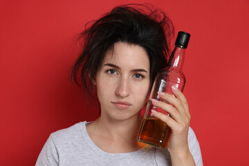 Woman with bottle of whiskey suffering from hangover on red background