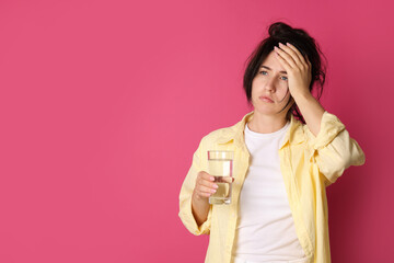 Woman with glass of water suffering from hangover on crimson background, space for text