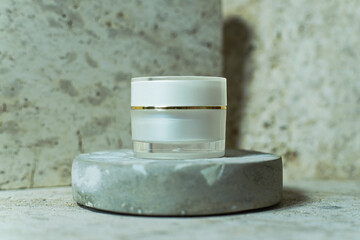 white cream jar placed on a stone pedestal with a marble background