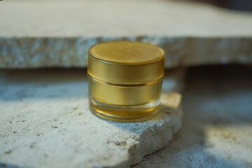 a golden cream jar stands on a pile of marble stones. Beauty concept