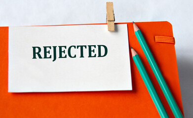 REJECTED - word on a white sheet on an orange notebook and pencils