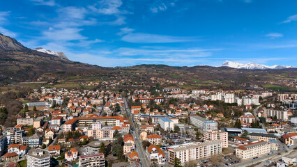 Drone view of the French city of Gap with residential buildings and snowy mountains on a clear day in March