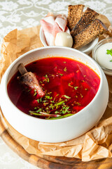 Traditional Ukrainian borscht with beef bone served with sour cream, rye bread, pork fat, onion, and herbs on a rustic wooden board.