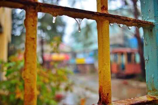 Rain drops clinging to rusty yellow metal bars, blurry background of colorful buildings - Powered by Adobe