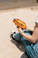 Hot dog held by young woman against beach scenery. Summer eating moment full of flavor and freedom.