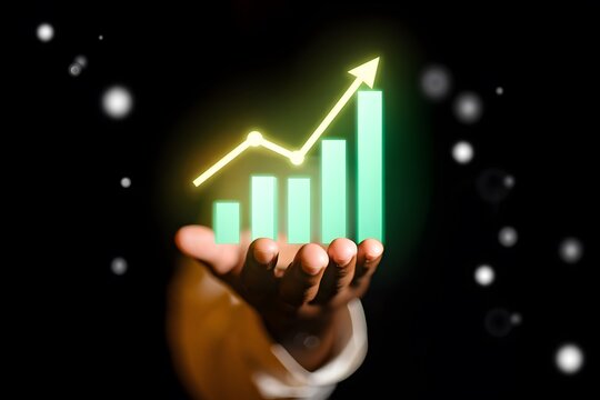 Hand holding a glowing green bar chart with an upward trending line symbolizing financial growth and success against a dark bokeh background