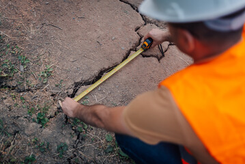 Construction worker measuring crack in ground with tape measure